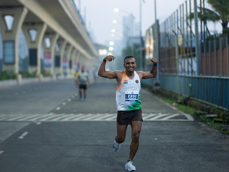 A half marathon runner raises both arms near the finish.